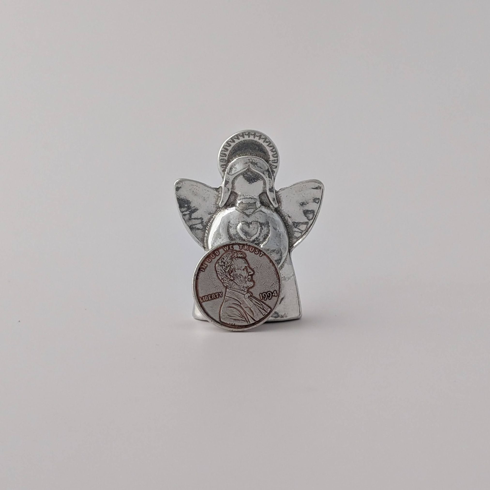 Silver angel figurine holding a penny on a light gray background