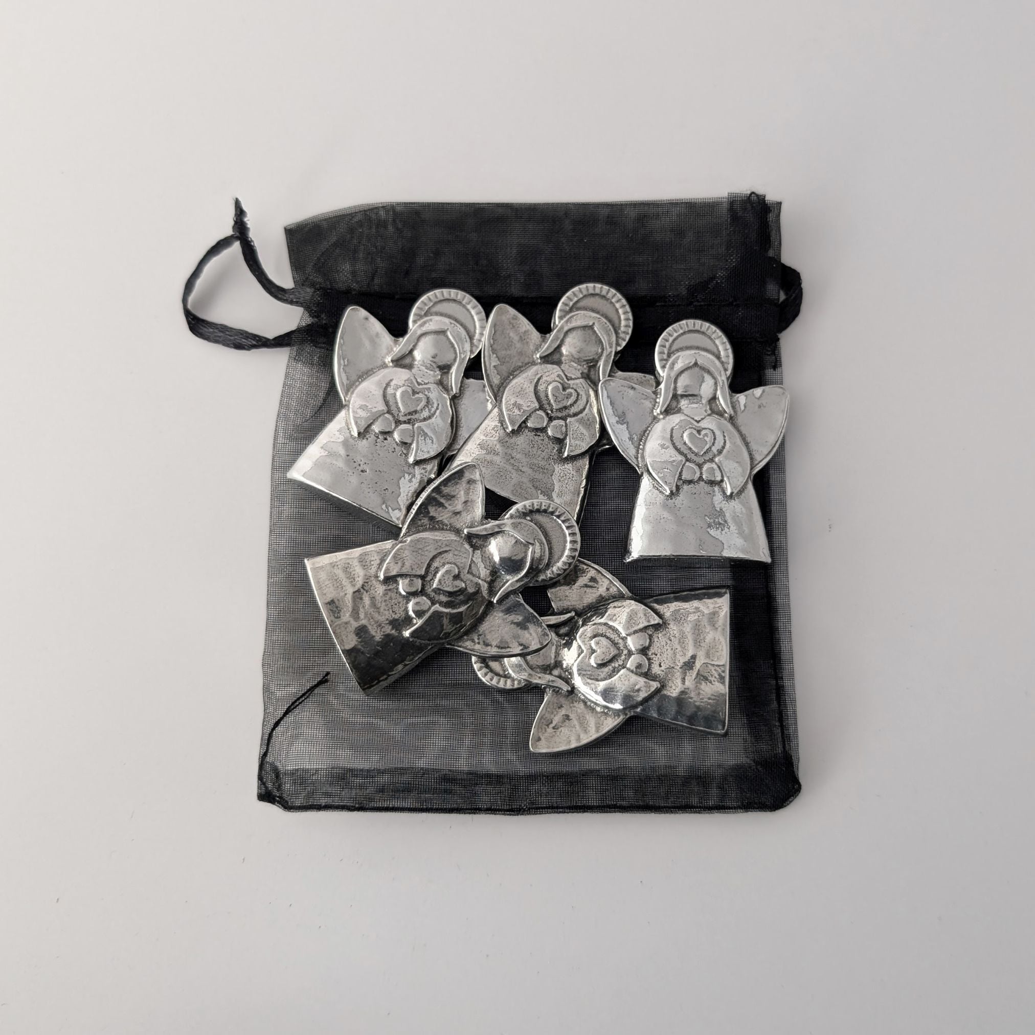 Set of silver angel-shaped pins in a black drawstring bag on a light gray background