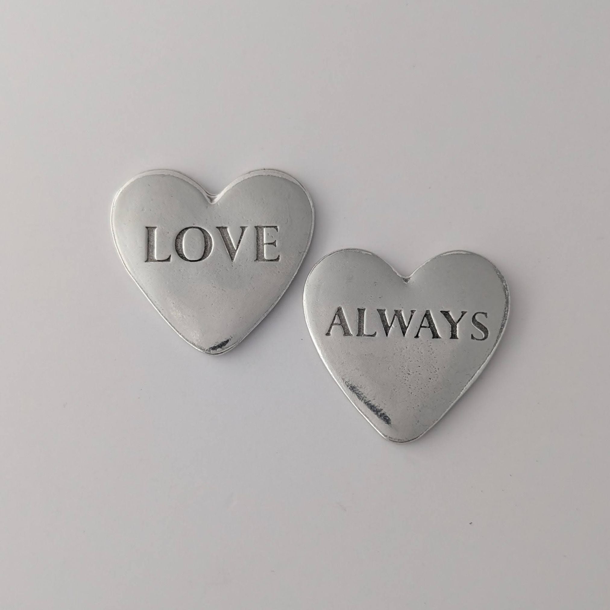 Two silver heart-shaped pendants with 'LOVE' and 'ALWAYS' engraved on a light gray background.