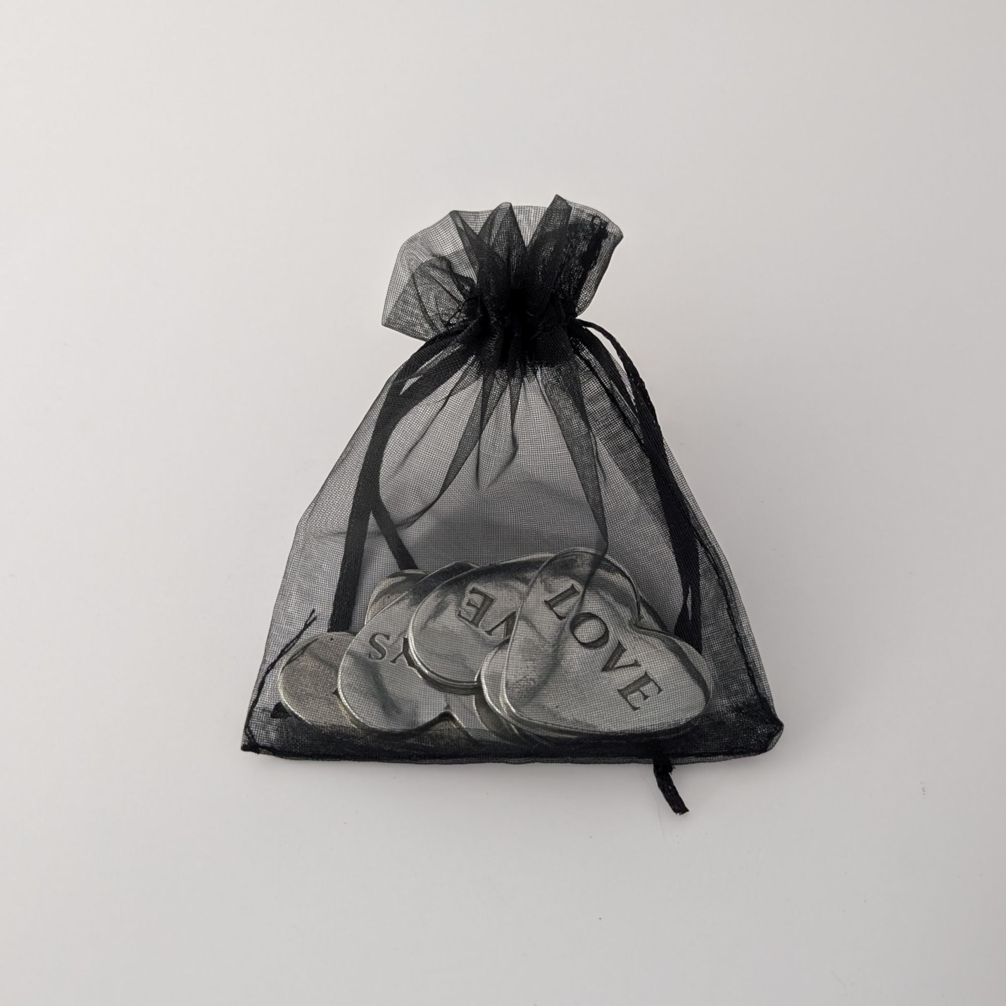 Black drawstring bag with heart-shaped metal tokens on a light gray background