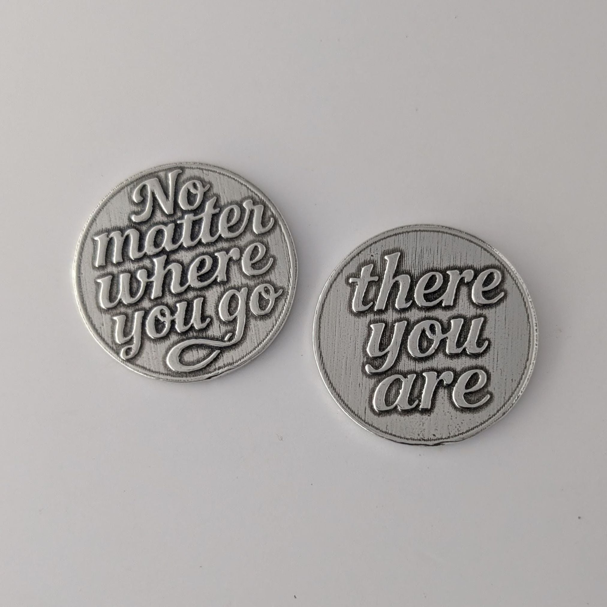 Two pewter tokens with engraved text on a gray background