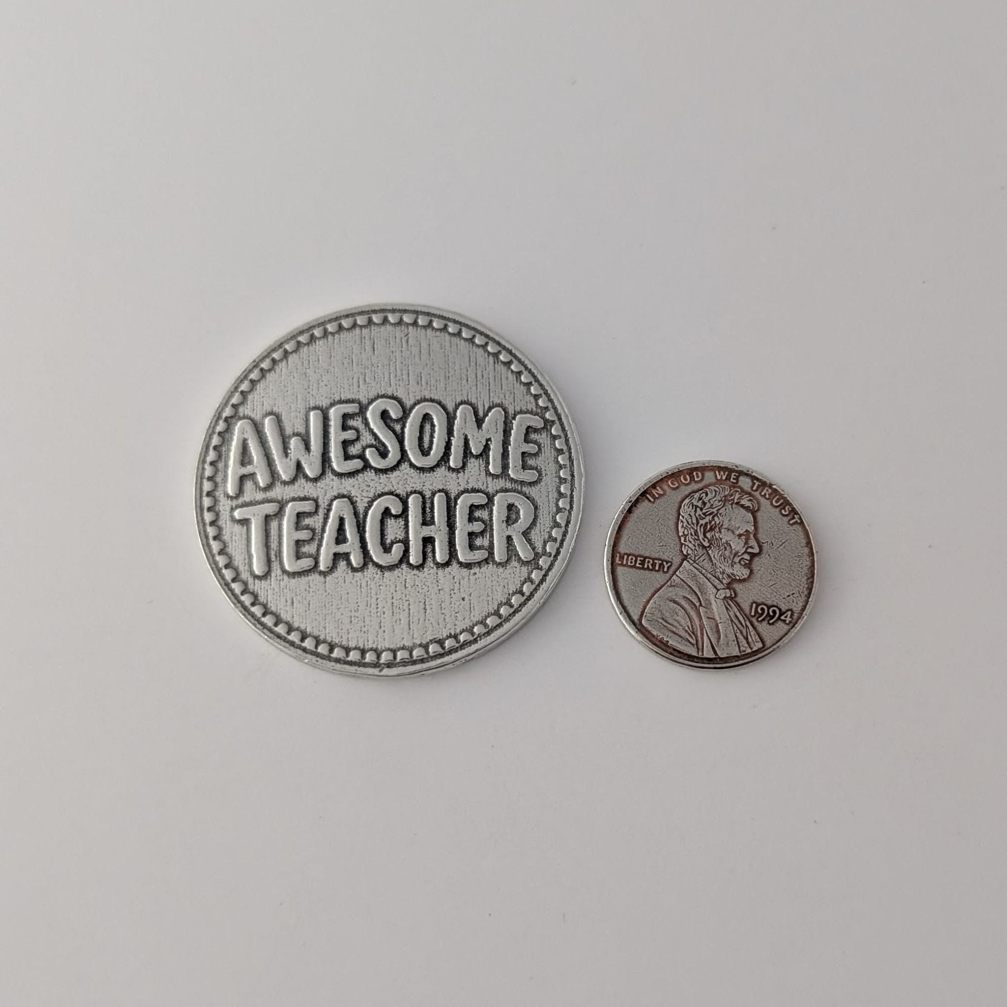 Pewter 'Awesome Teacher' coin next to a penny on a light gray background