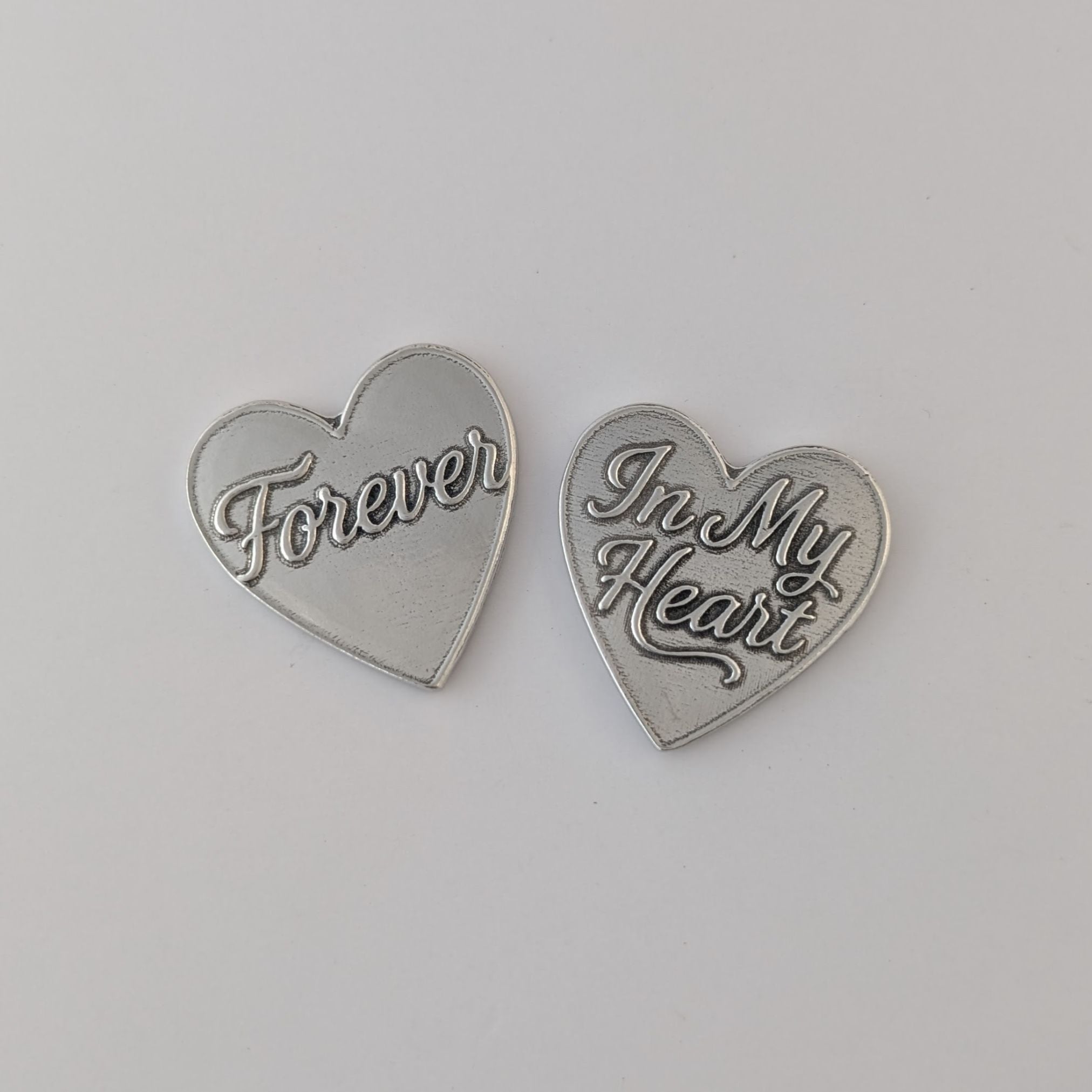 Two silver heart-shaped pendants with engraved text on a light gray background