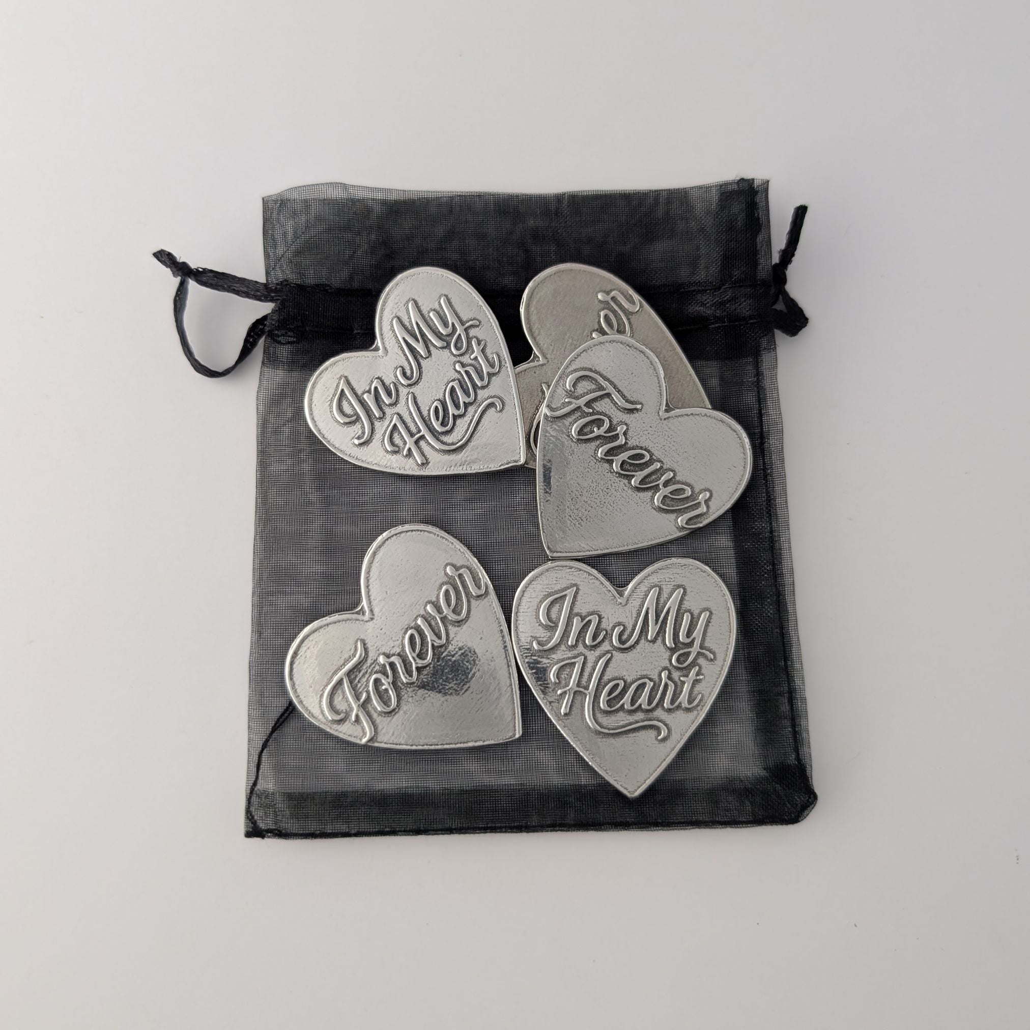 Four metallic heart-shaped pendants with engraved text on a black drawstring bag.
