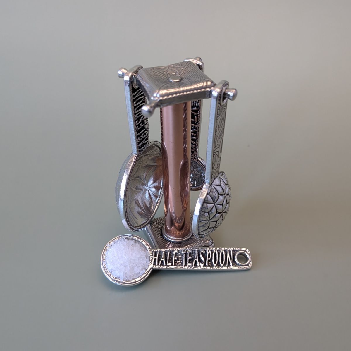 Pewter measuring spoons on copper stand- green background