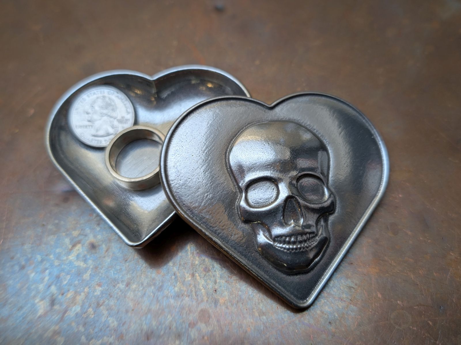 Heart-shaped metal object with skull design on a textured surface