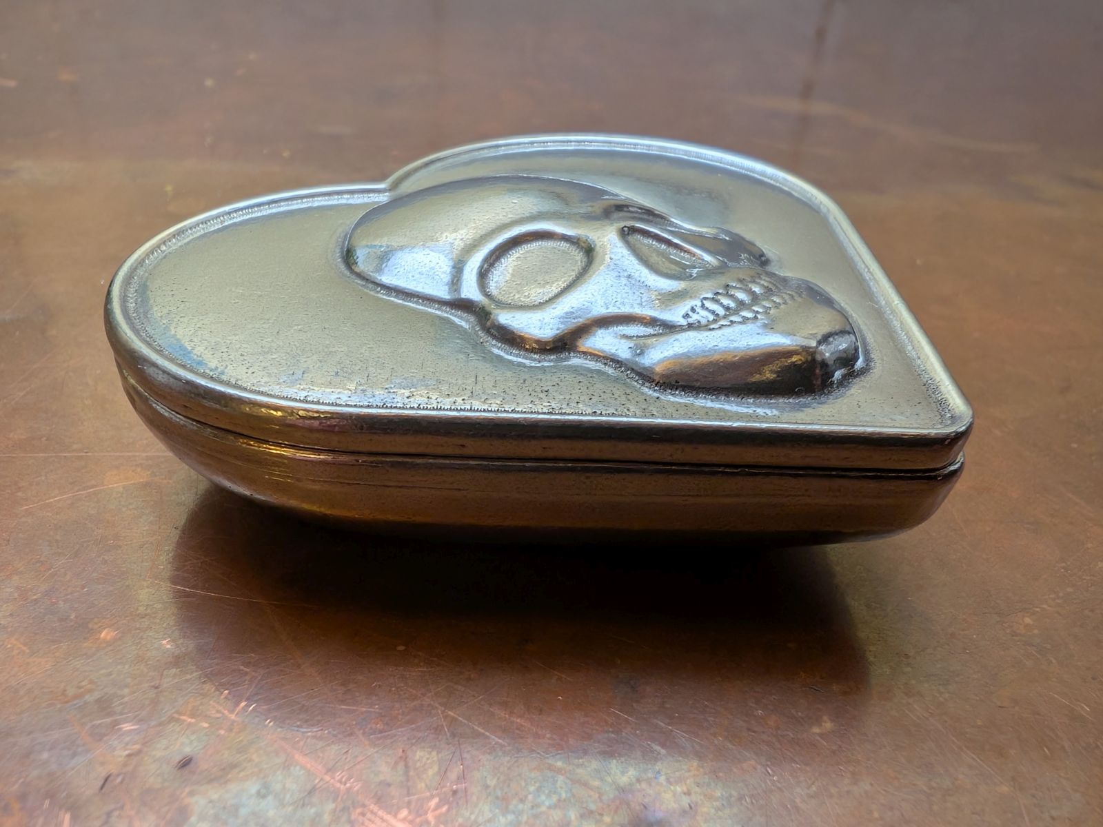 Heart-shaped pewter box with skull design on a copper surface