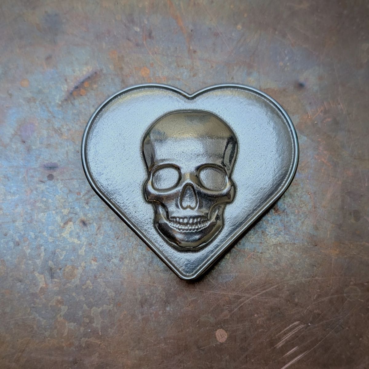 Metallic skull design in a heart shaped pewter box on a textured metal surface