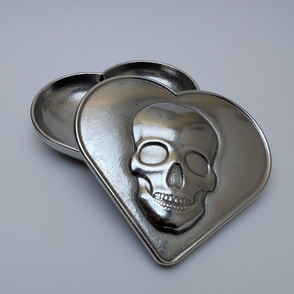 Heart-shaped metal container with skull design on a gray background