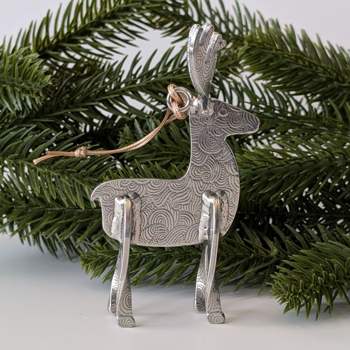 Silver deer ornament on a branch with a white background