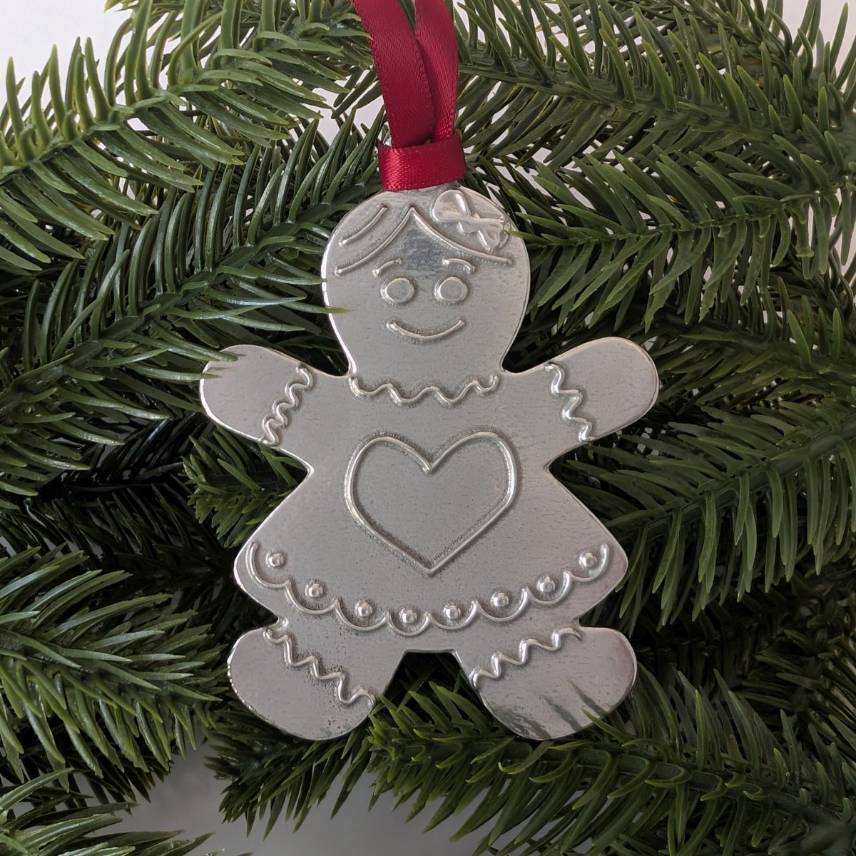 Silver gingerbread girl ornament with a red ribbon on a Christmas tree.