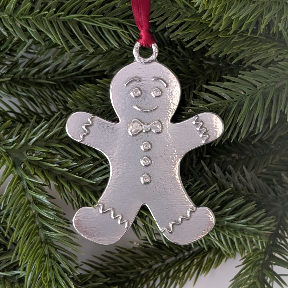Silver gingerbread man ornament on a red ribbon against a green Christmas tree background