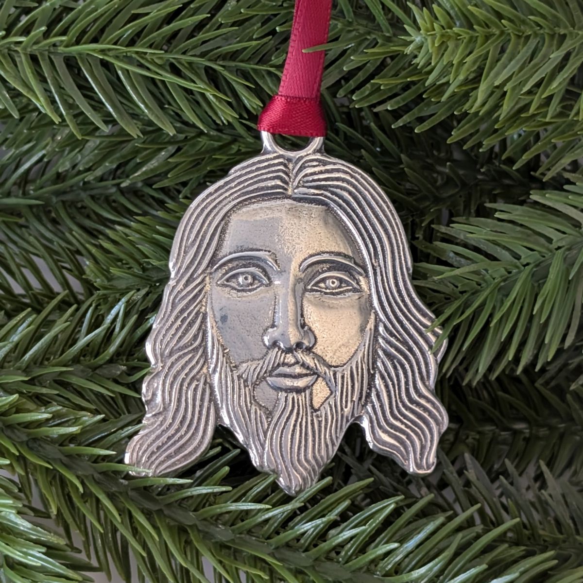 Decorative ornament with Jesus face design on a green pine branch.