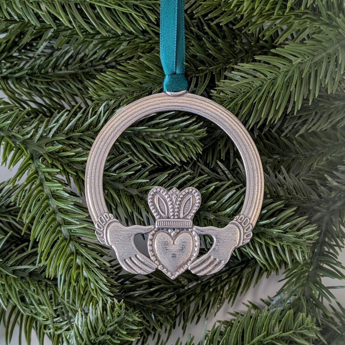 Decorative Claddagh ring ornament on a green ribbon against a green leafy background