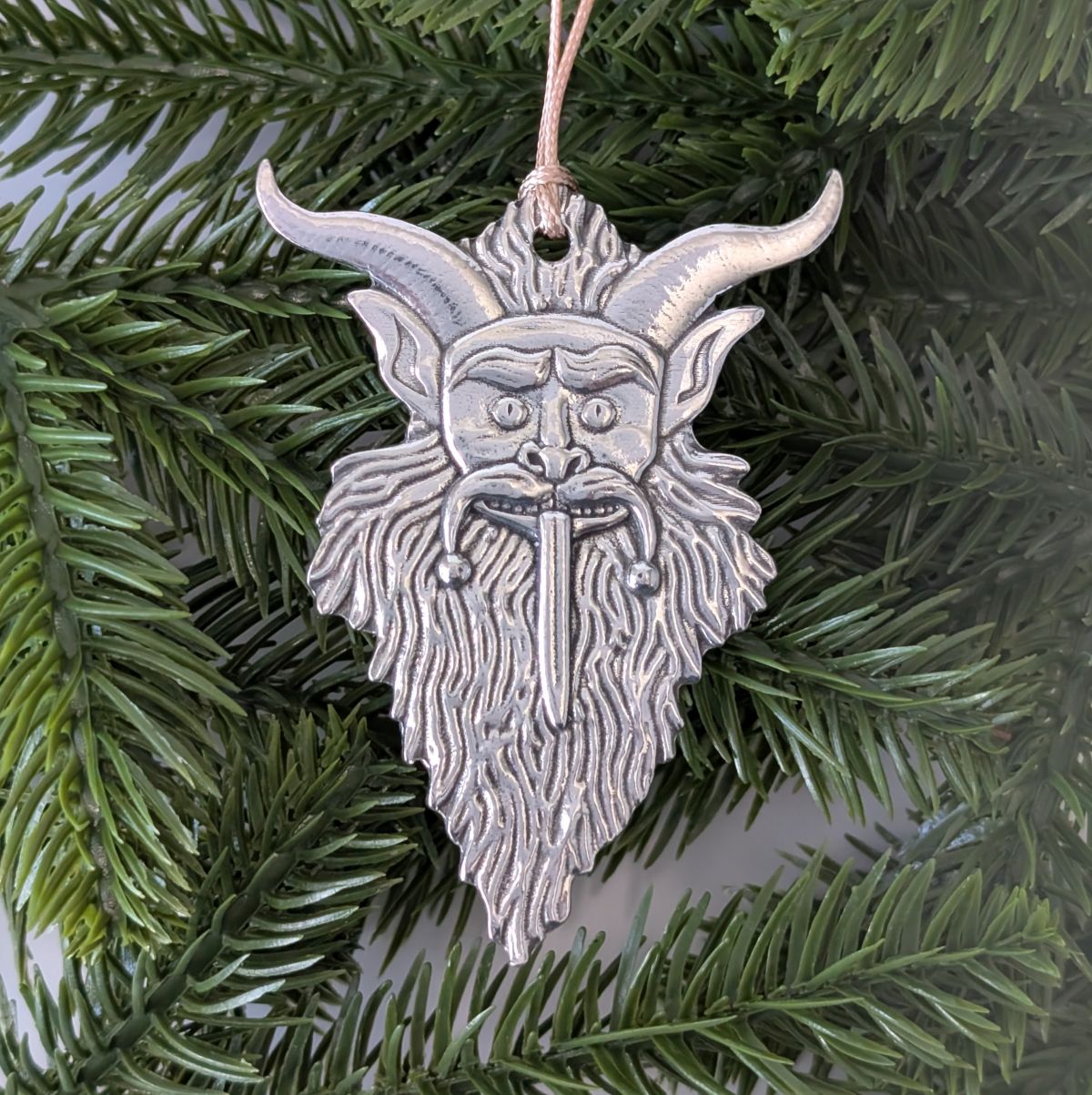 Silver goat head ornament hanging on a green pine branch