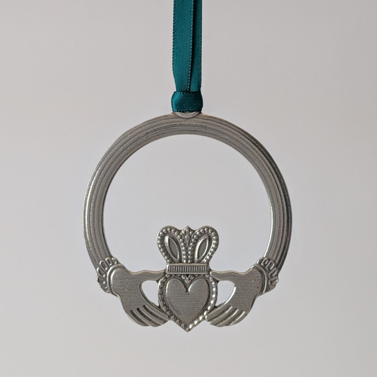 Silver Claddagh ring ornament with a green ribbon on a light gray background