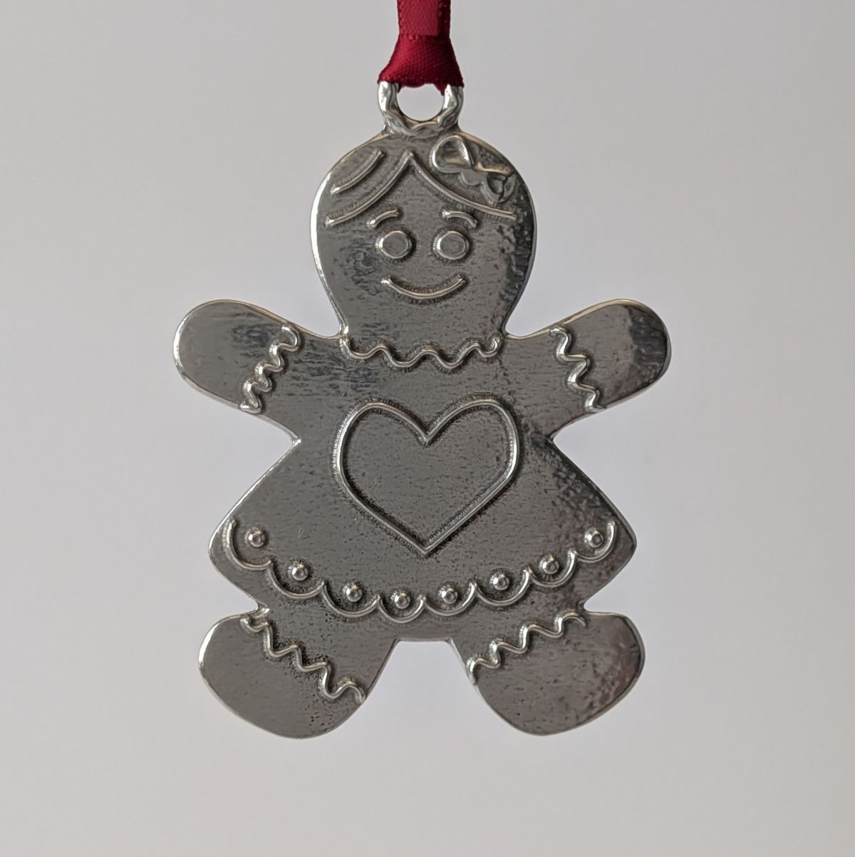 Metallic gingerbread woman ornament with a heart on a plain background