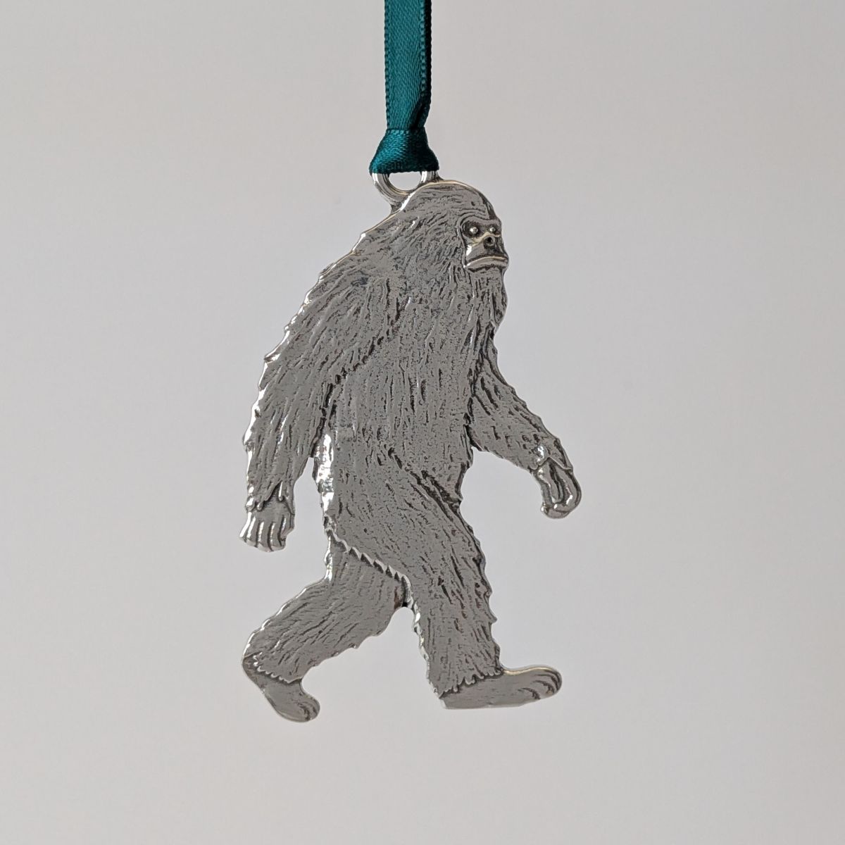 Metallic Bigfoot ornament on a green ribbon against a light gray background