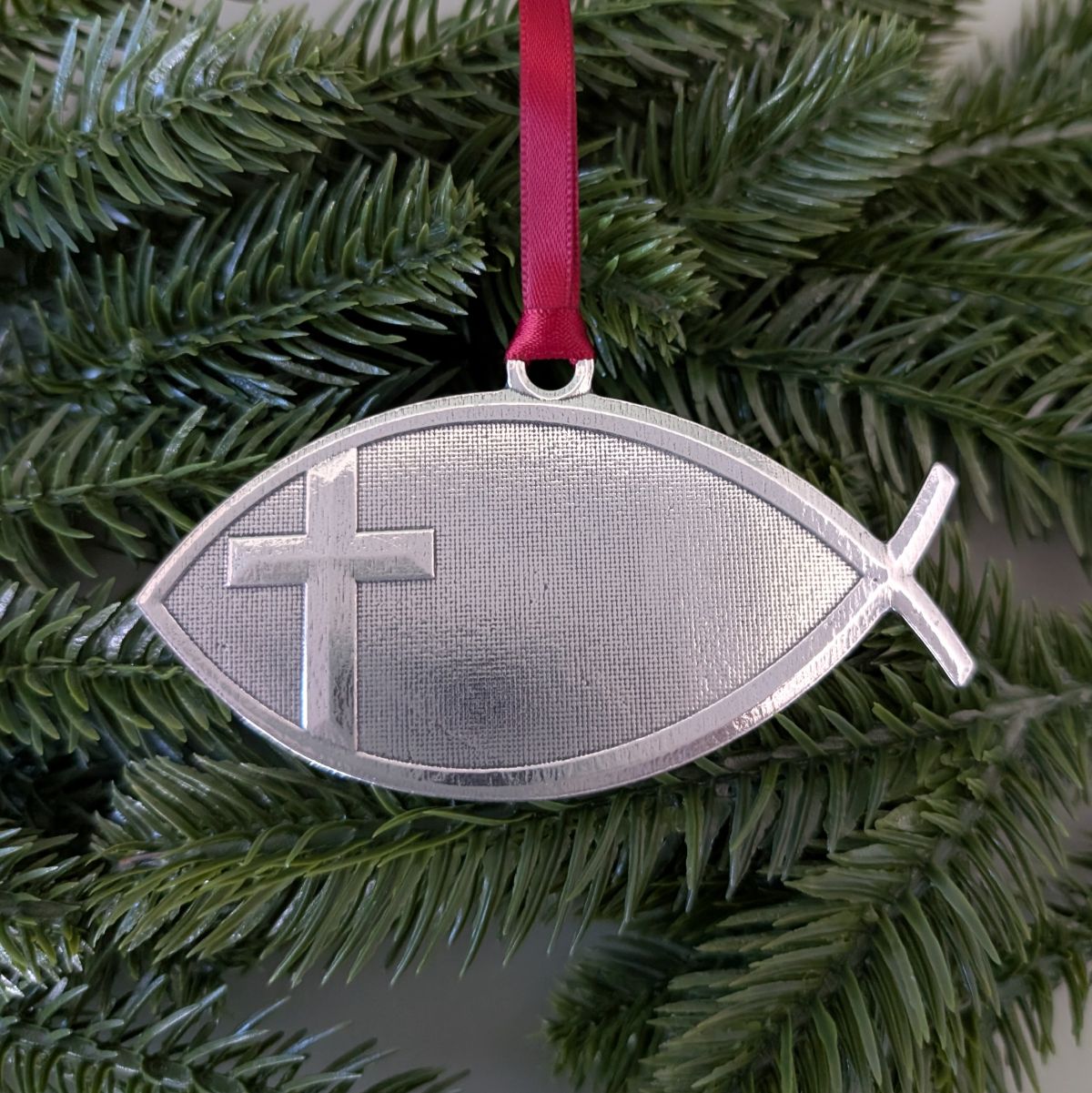 Decorative ornament shaped like a fish with a cross on a green branch