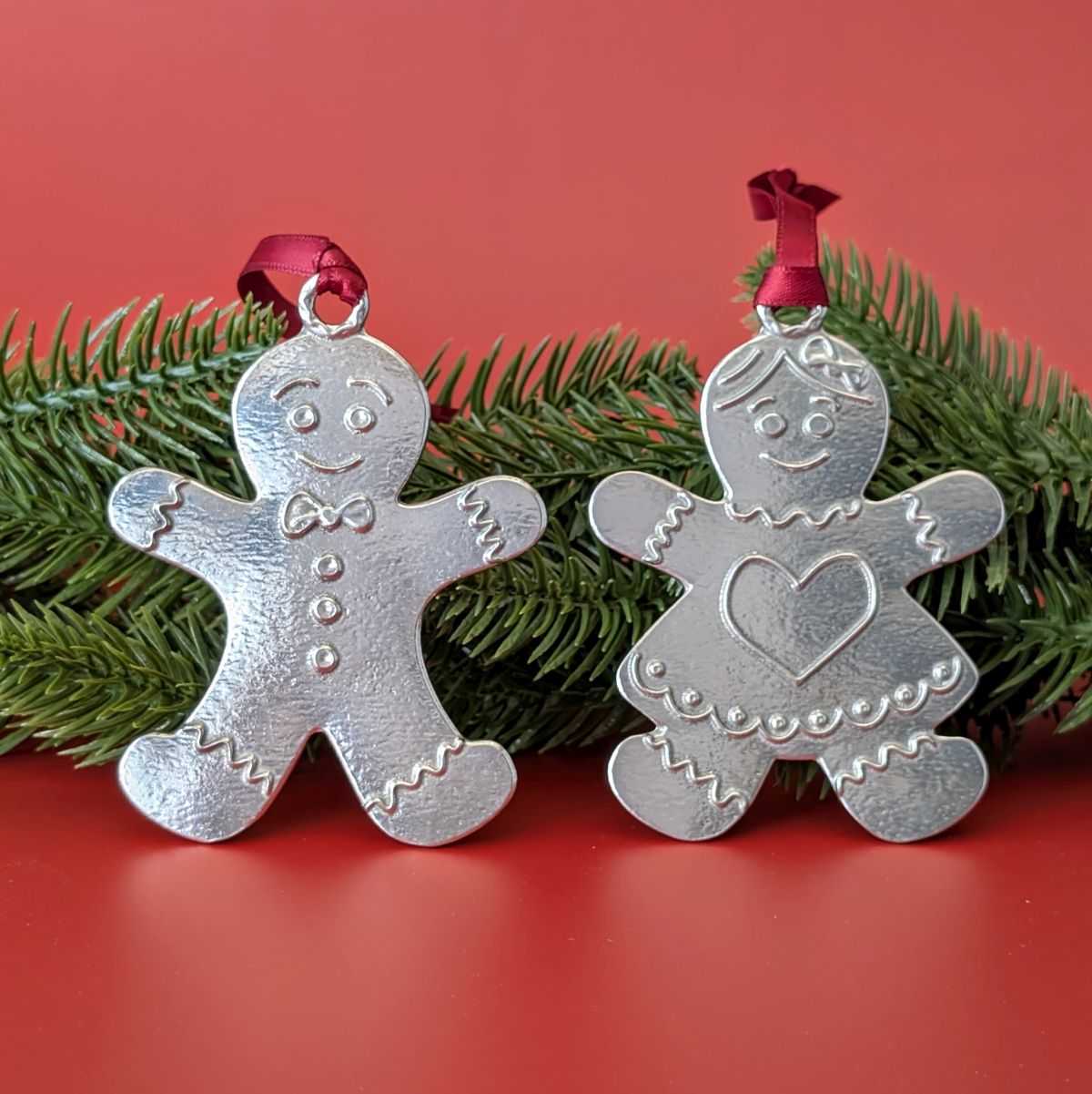 Two silver gingerbread people vornaments with red ribbons on a red background