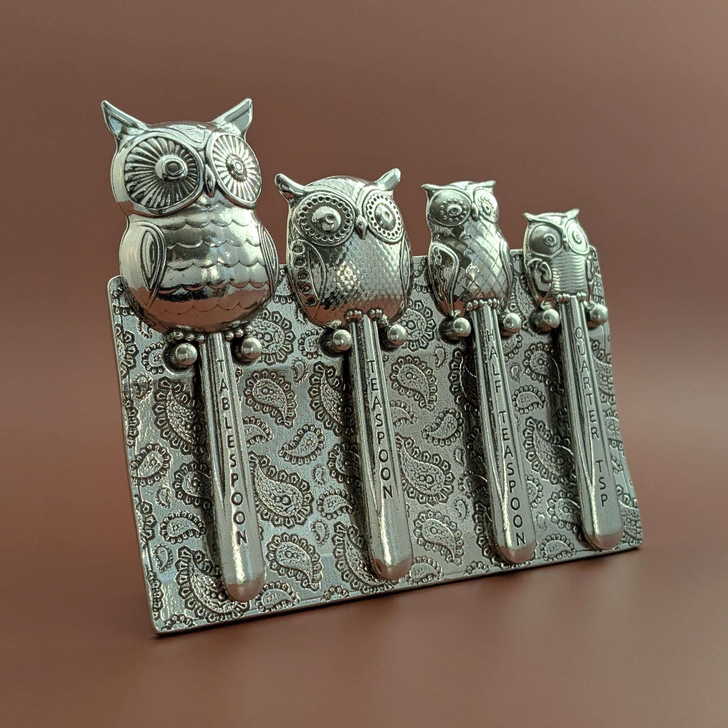 Pewter owl measuring spoons on wood