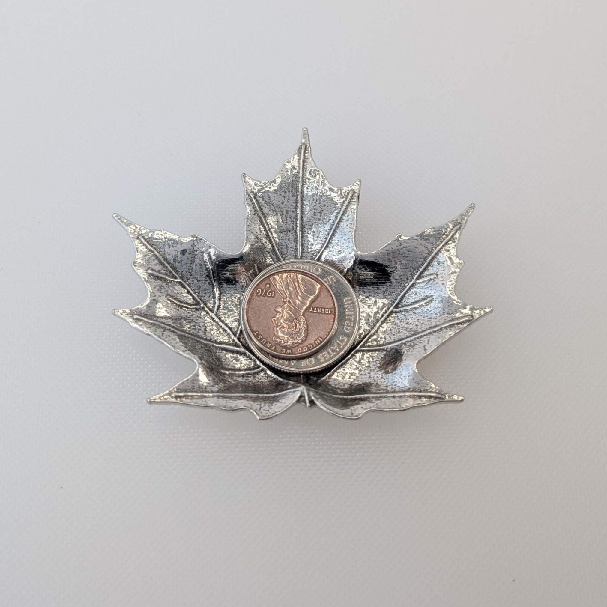 Pewter maple leaf dish on white surface