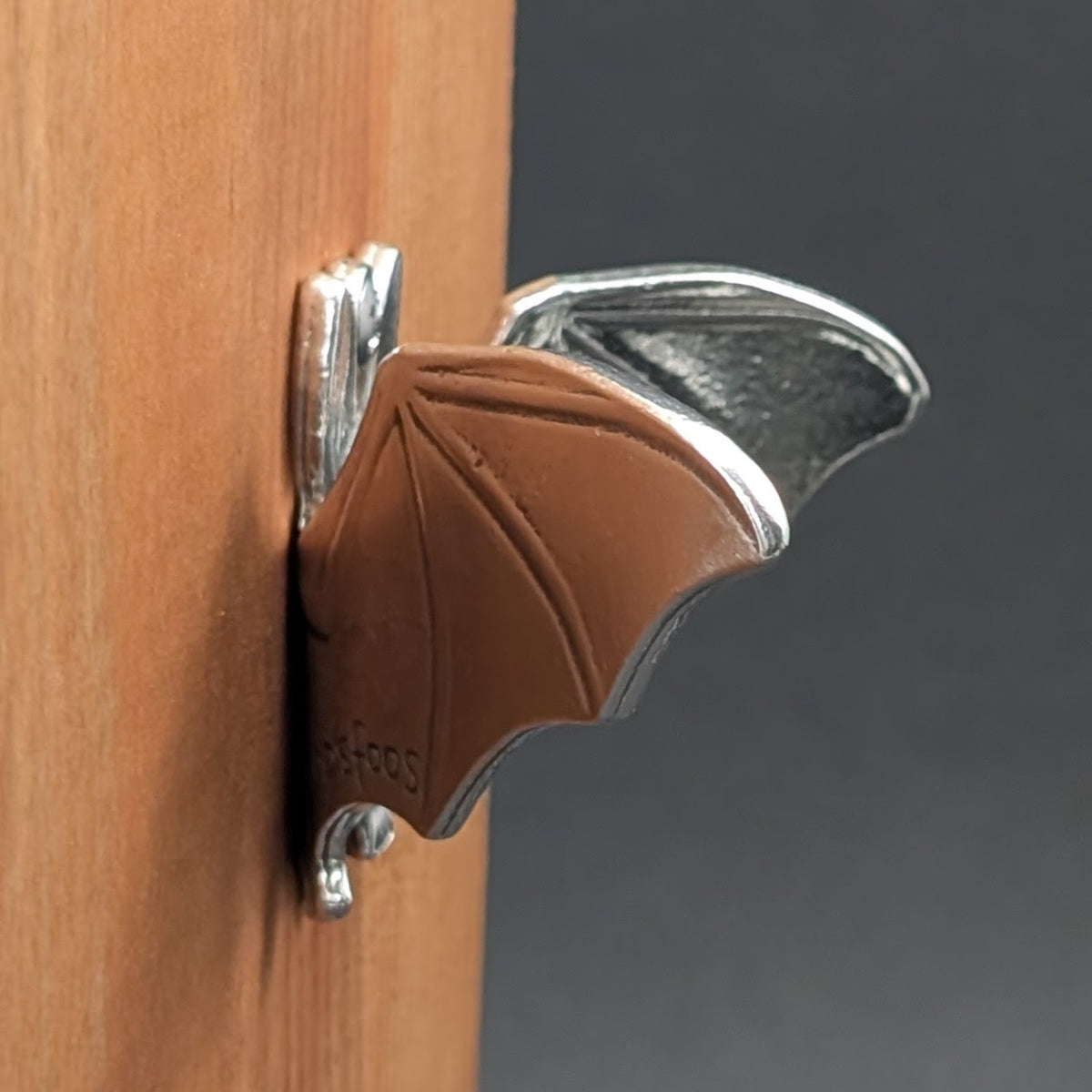 Close-up side view of a pewter bat wall hook wing detail mounted on wood