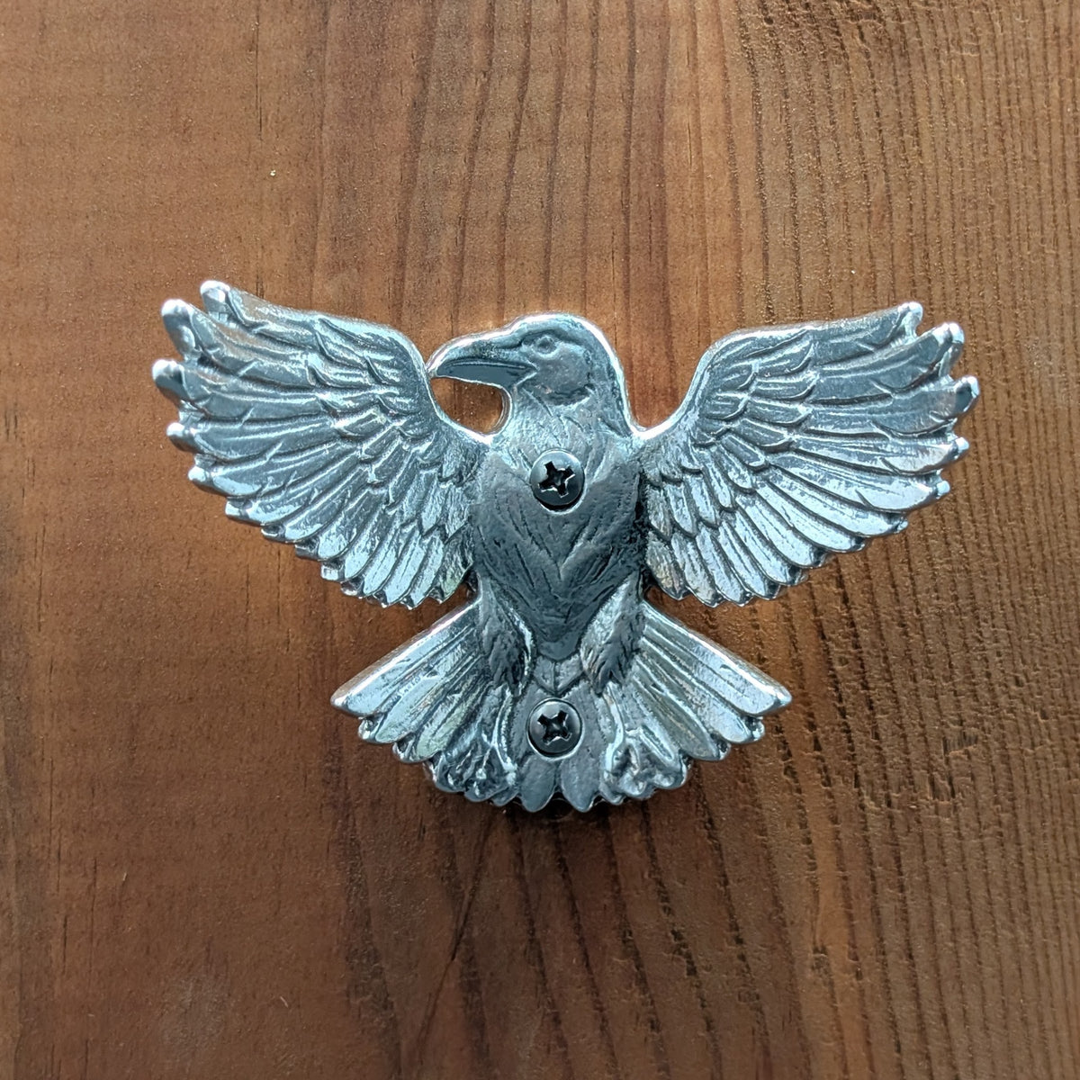 Pewter crow wall hook mounted on a wood board, front view