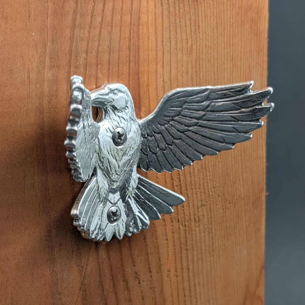 Pewter crow wall hook mounted on a wood board, angled close-up