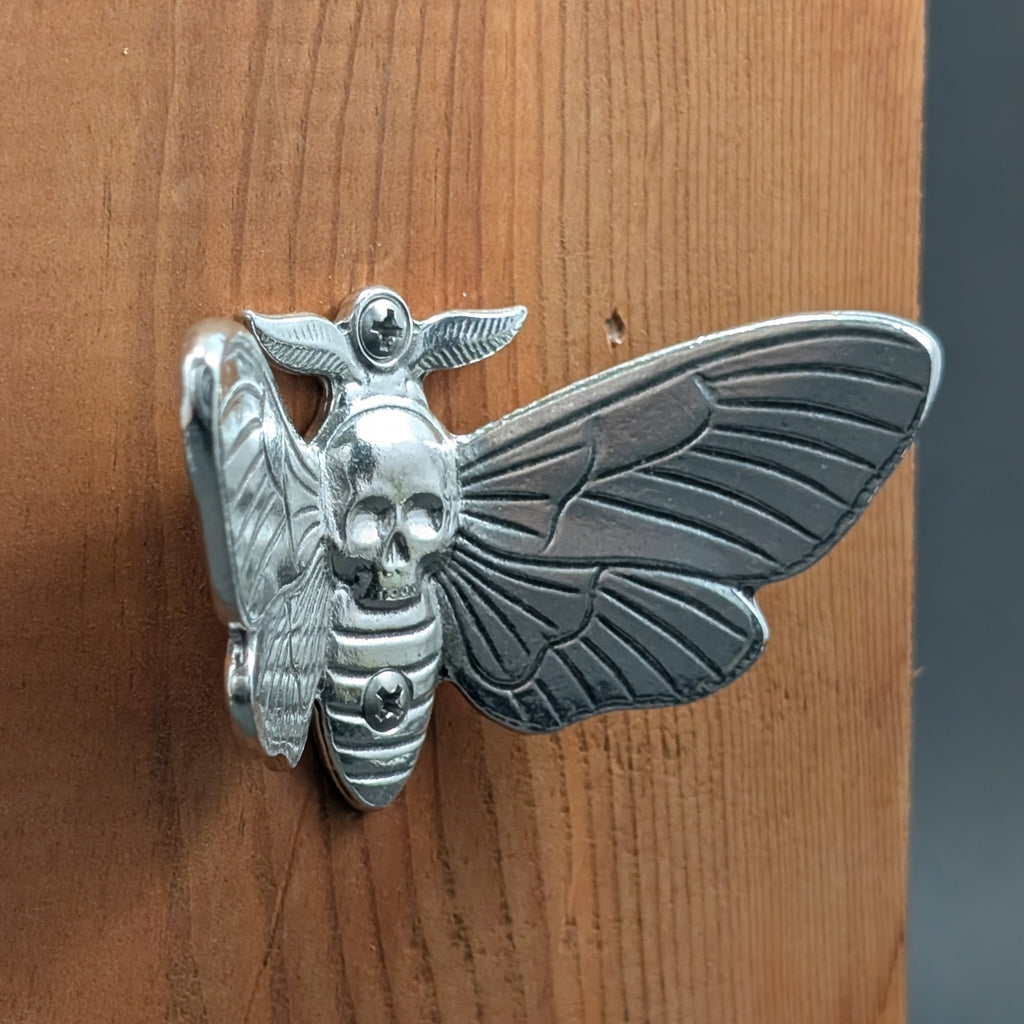 Pewter death's head hawkmoth wall hook mounted on a wood board, angled close-up
