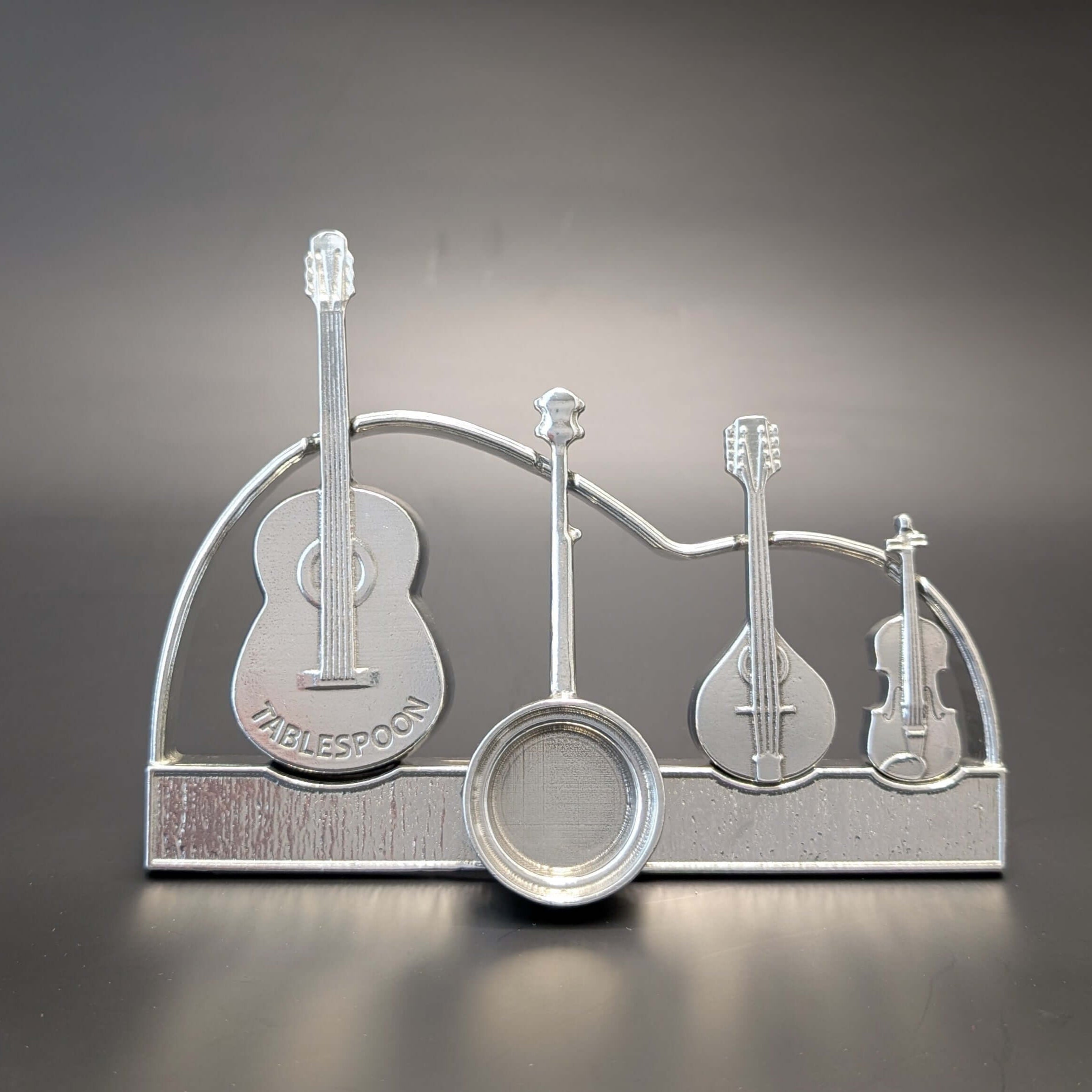 Pewter instrument guitar spoons on display stand. Guitar, banjo, mandolin, fiddle. Black background
