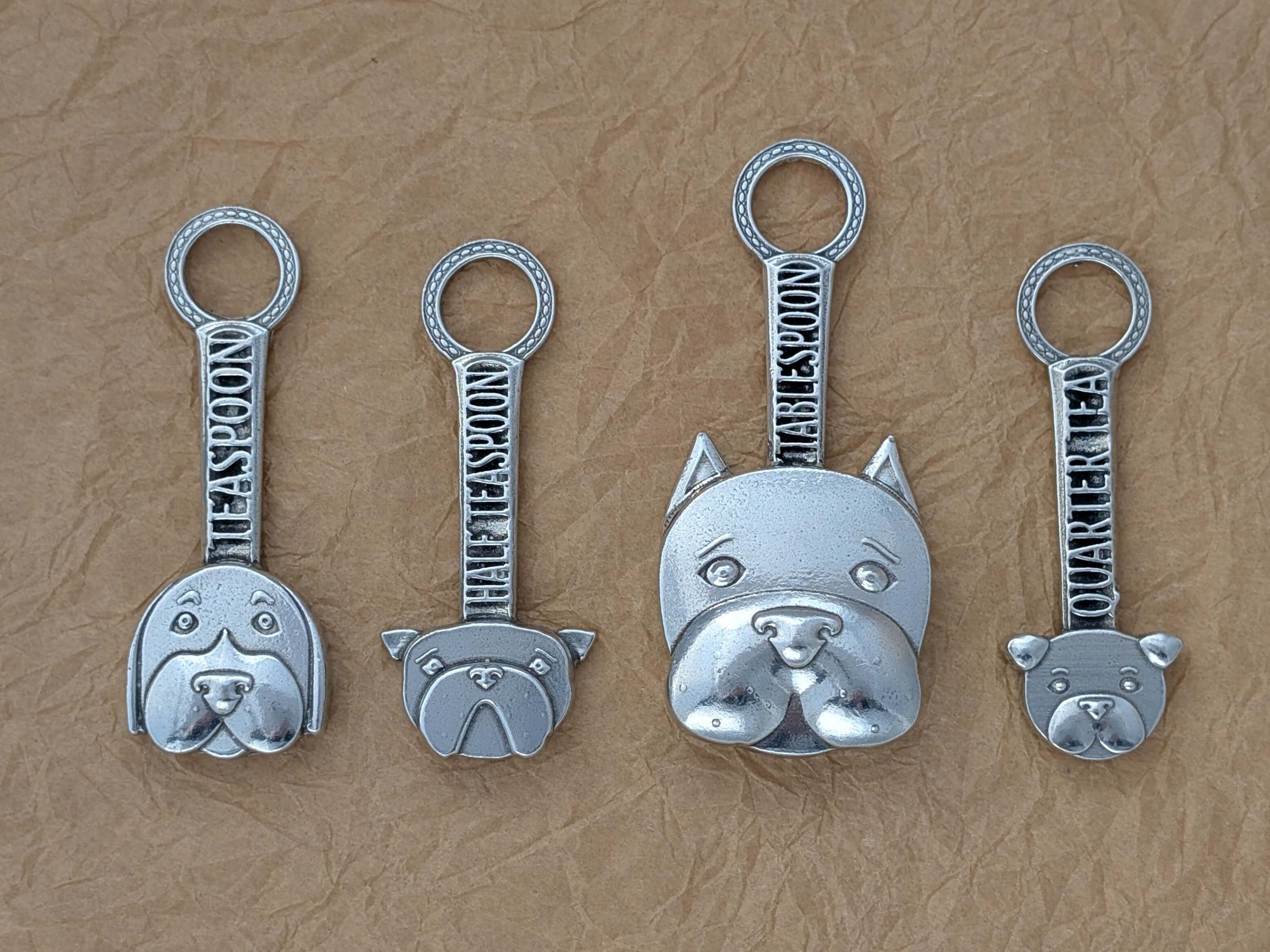 Pewter dog measuring spoons on brown surface