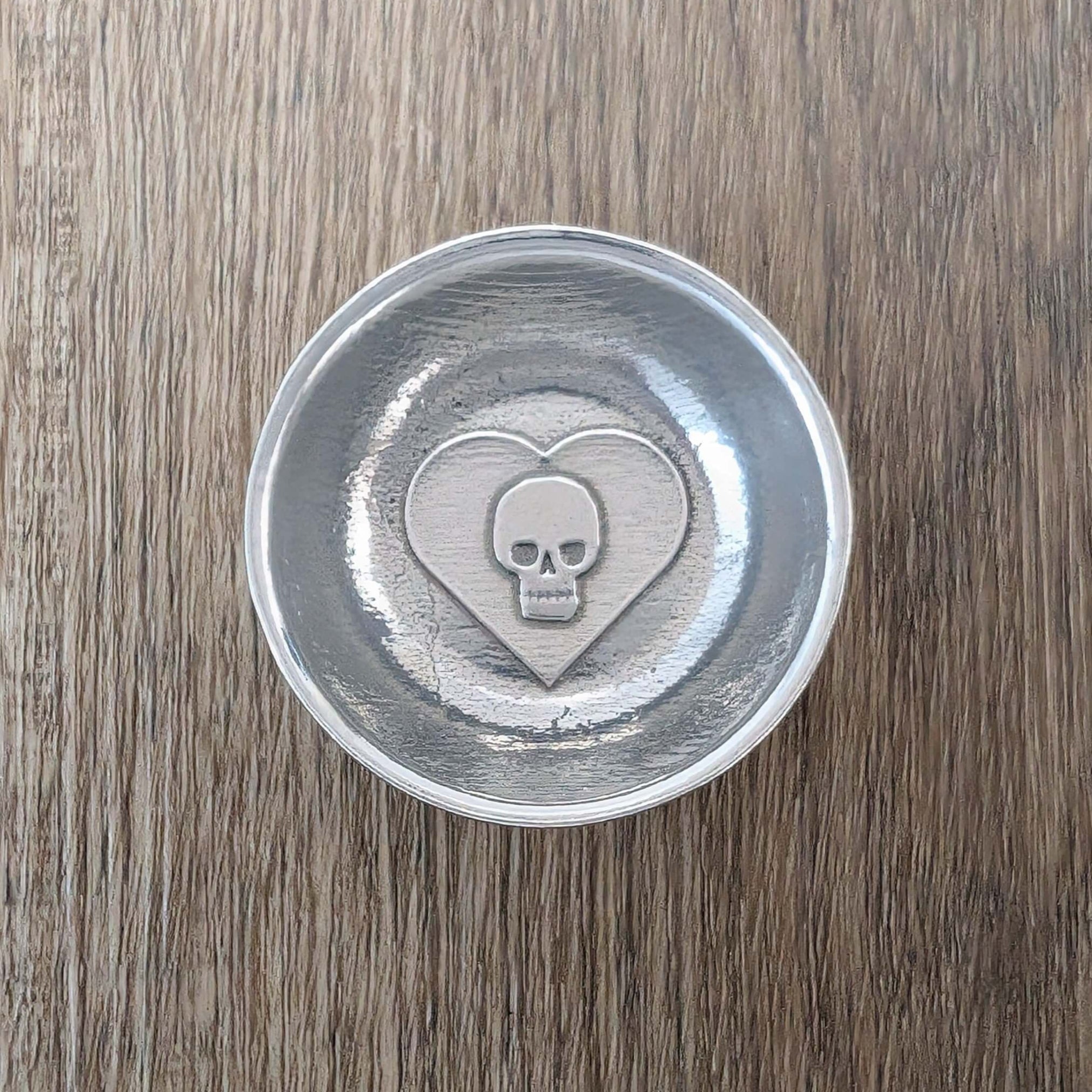 Skull in heart pewter ring dish on wood surface.
