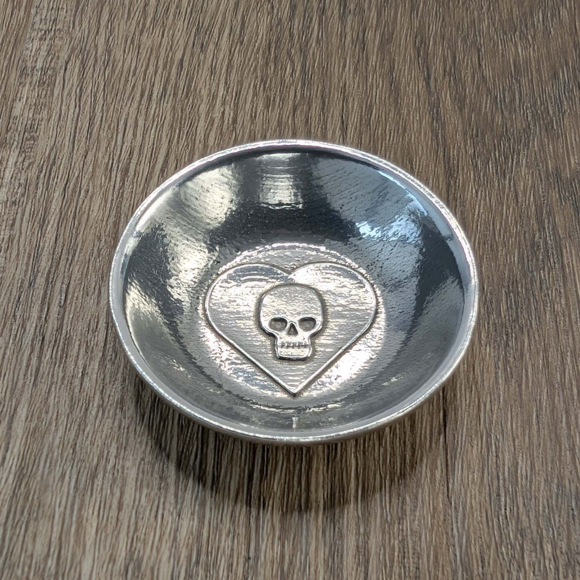 Skull in heart pewter ring dish on wood surface.