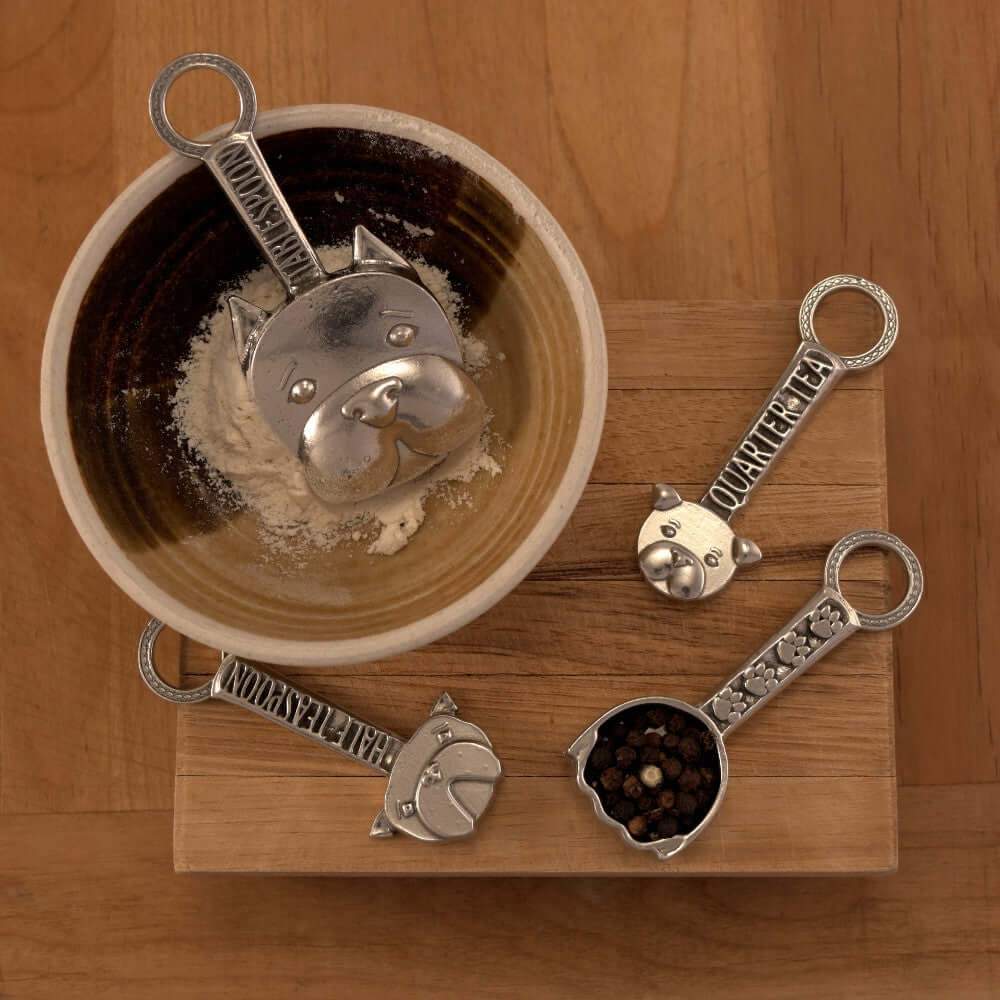 Pewter dog measuring spoons on wooden surface