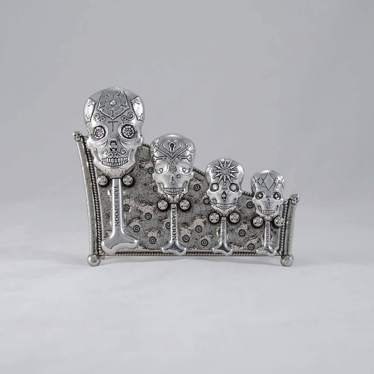 Pewter skull measuring spoons on display stand. White background
